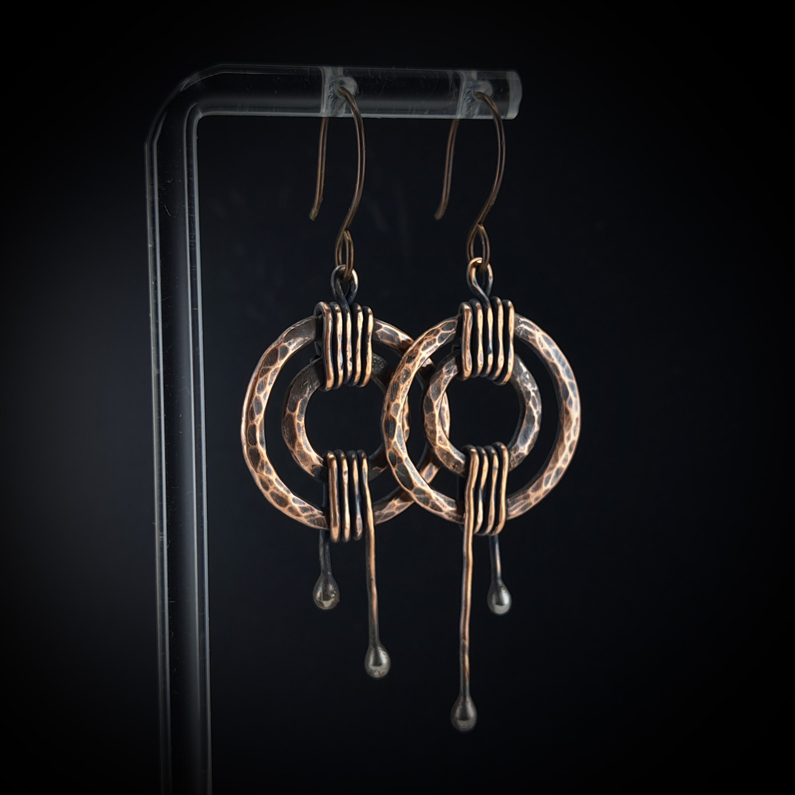 Hammered copper double ring earrings on black acrylic stand — oxidized finish, side view