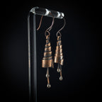 Copper spiral earrings on acrylic stand, black background — side view