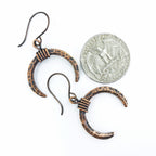 Lunar Horns copper crescent earrings next to a quarter coin for size reference — approximately 1 inch wide