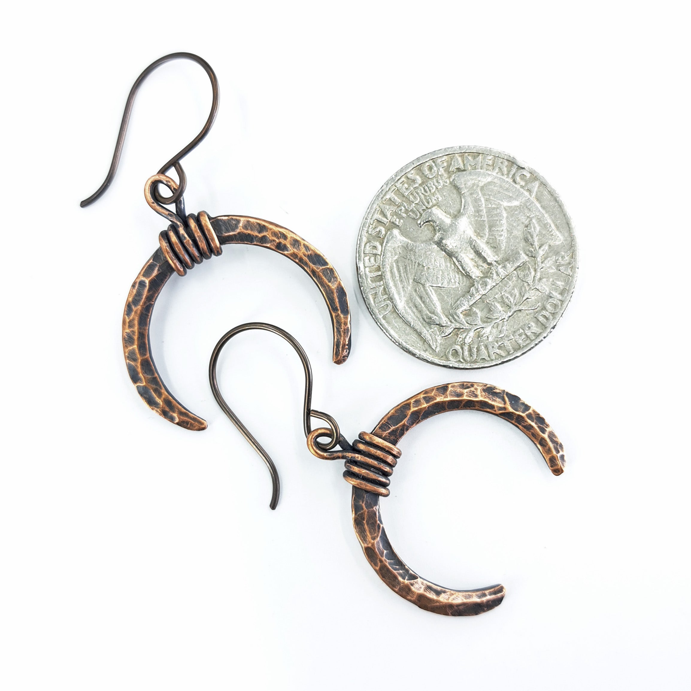 Lunar Horns copper crescent earrings next to a quarter coin for size reference — approximately 1 inch wide