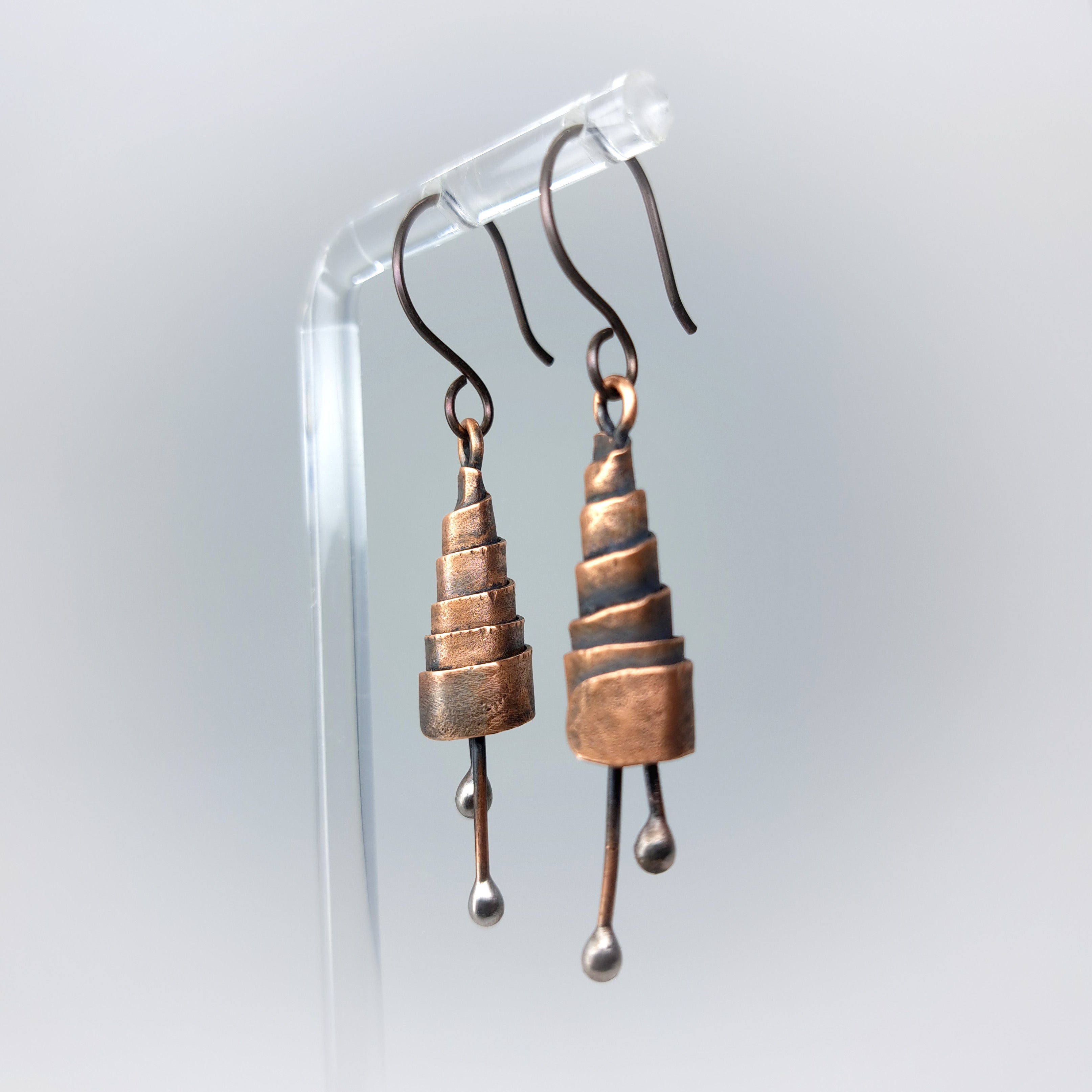 Pair of copper spiral earrings on a clear stand against a light gray background