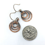 Small hammered copper ring earrings next to a quarter coin for size reference — smaller than a quarter, handmade.