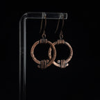 Copper open ring earrings on acrylic stand, dark background, side angle — Torque