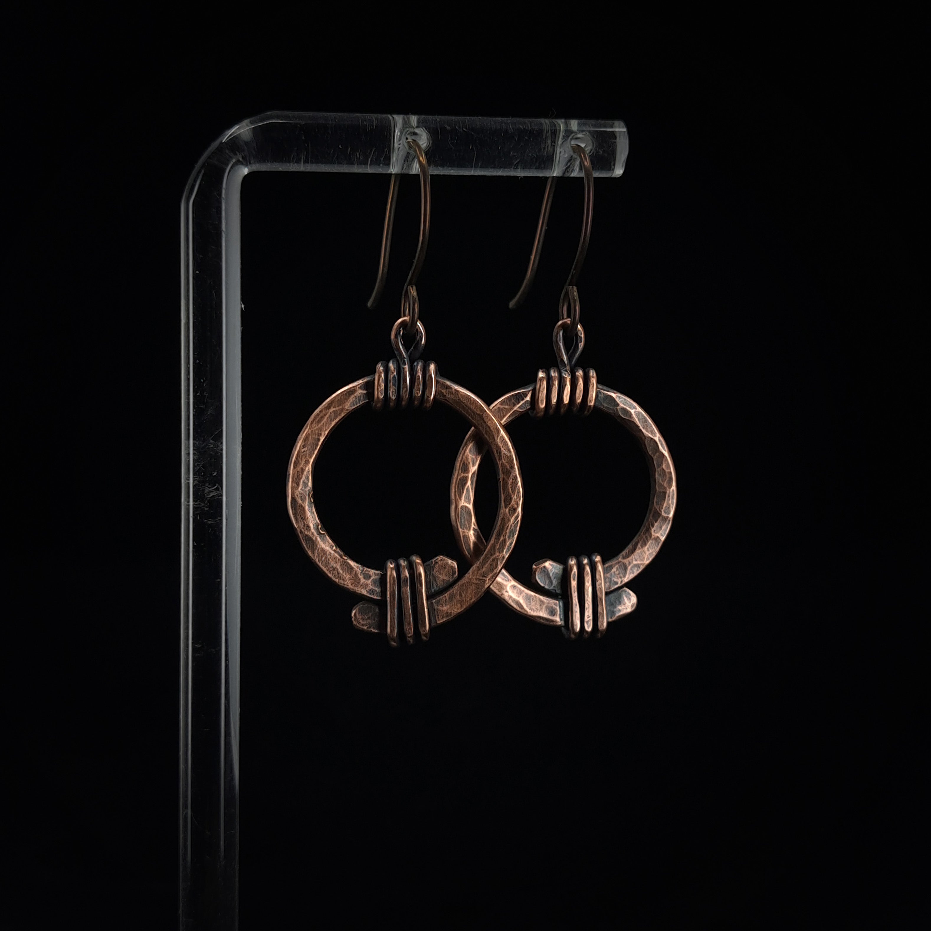Copper open ring earrings on acrylic stand, dark background, side angle — Torque