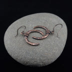 Lunar Horns copper crescent earrings on natural stone surface — showing hammered texture and oxidized finish