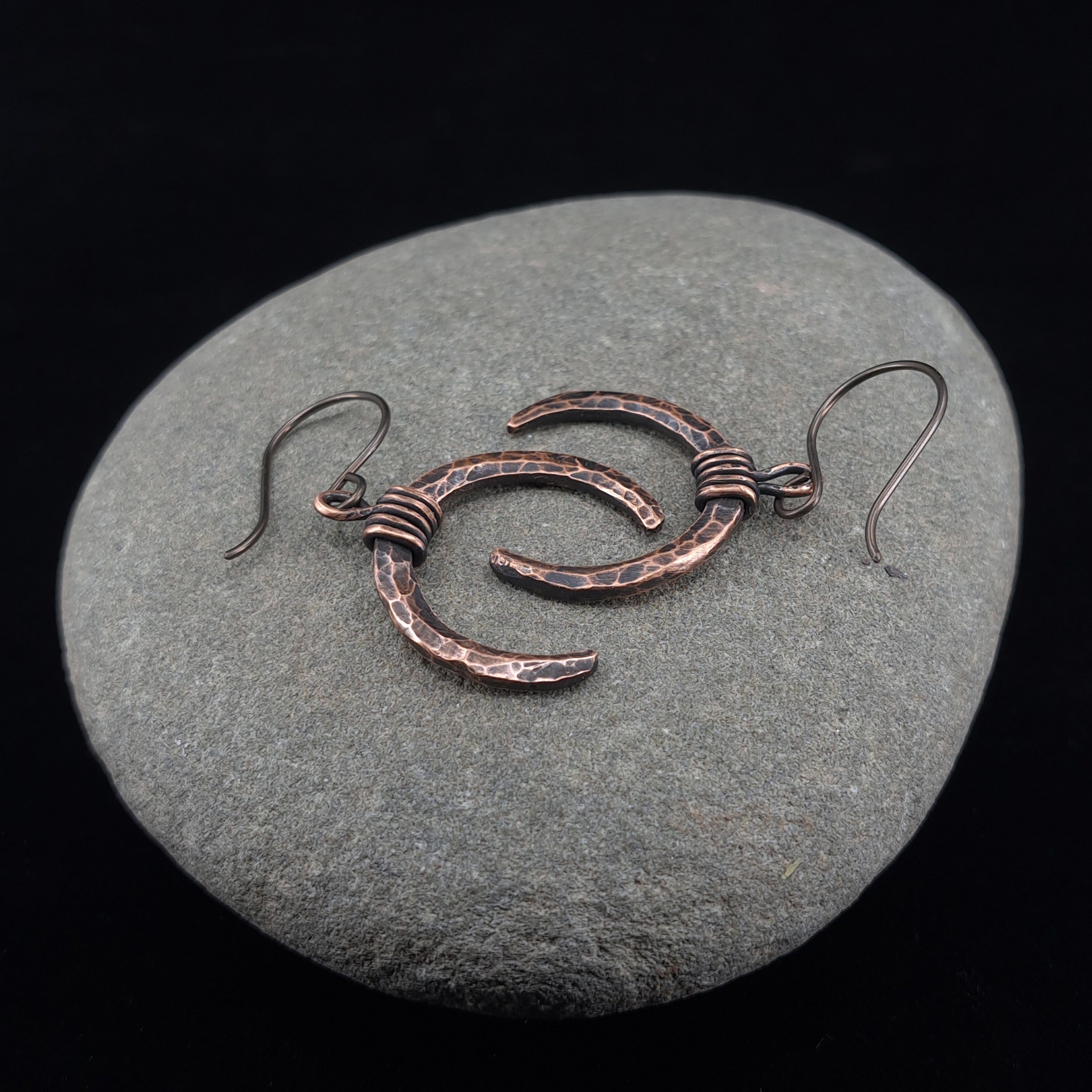 Lunar Horns copper crescent earrings on natural stone surface — showing hammered texture and oxidized finish