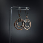 Copper double hoop earrings on acrylic stand — gray background