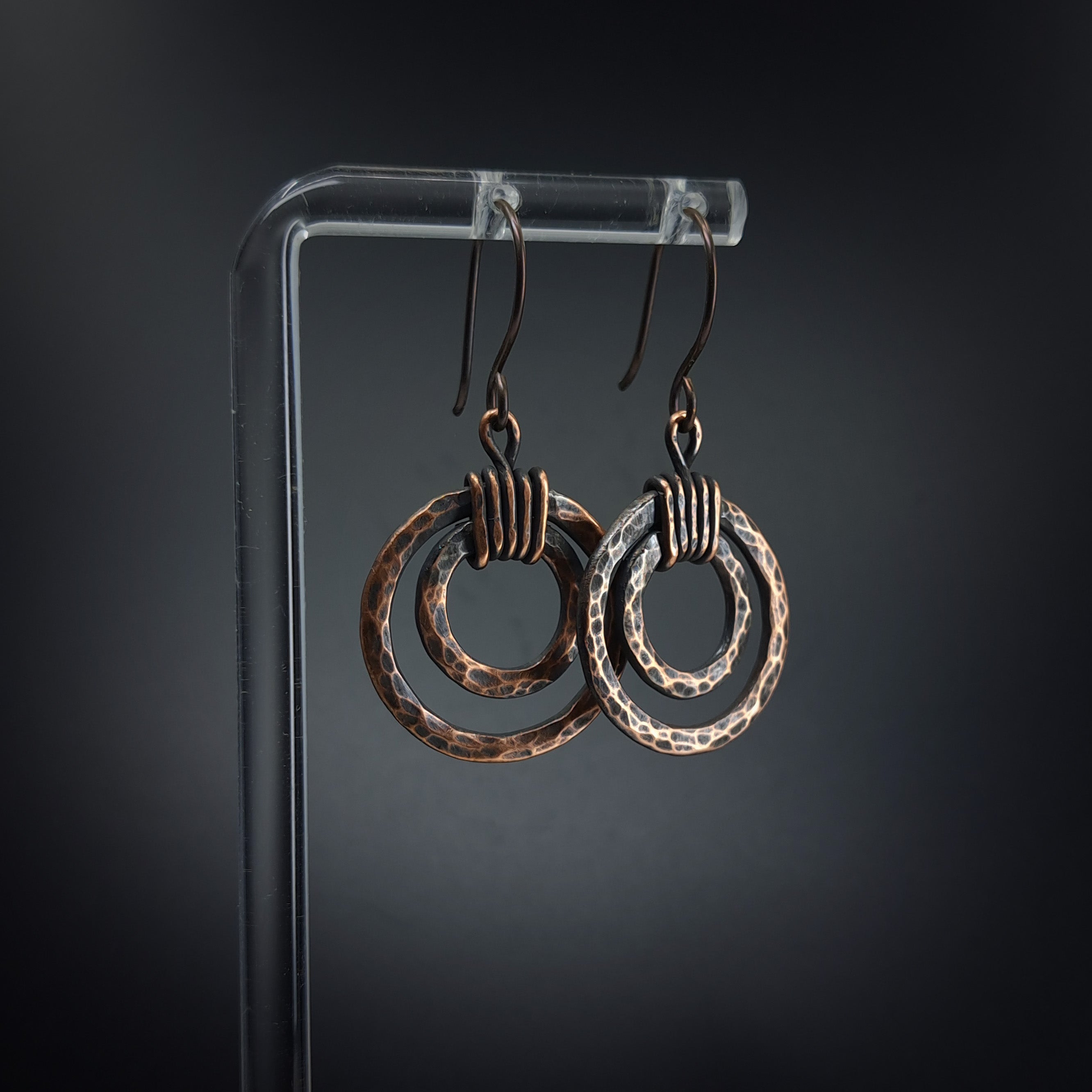 Copper double hoop earrings on acrylic stand — gray background