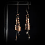 Copper spiral earrings close-up, black background — oxidized copper texture