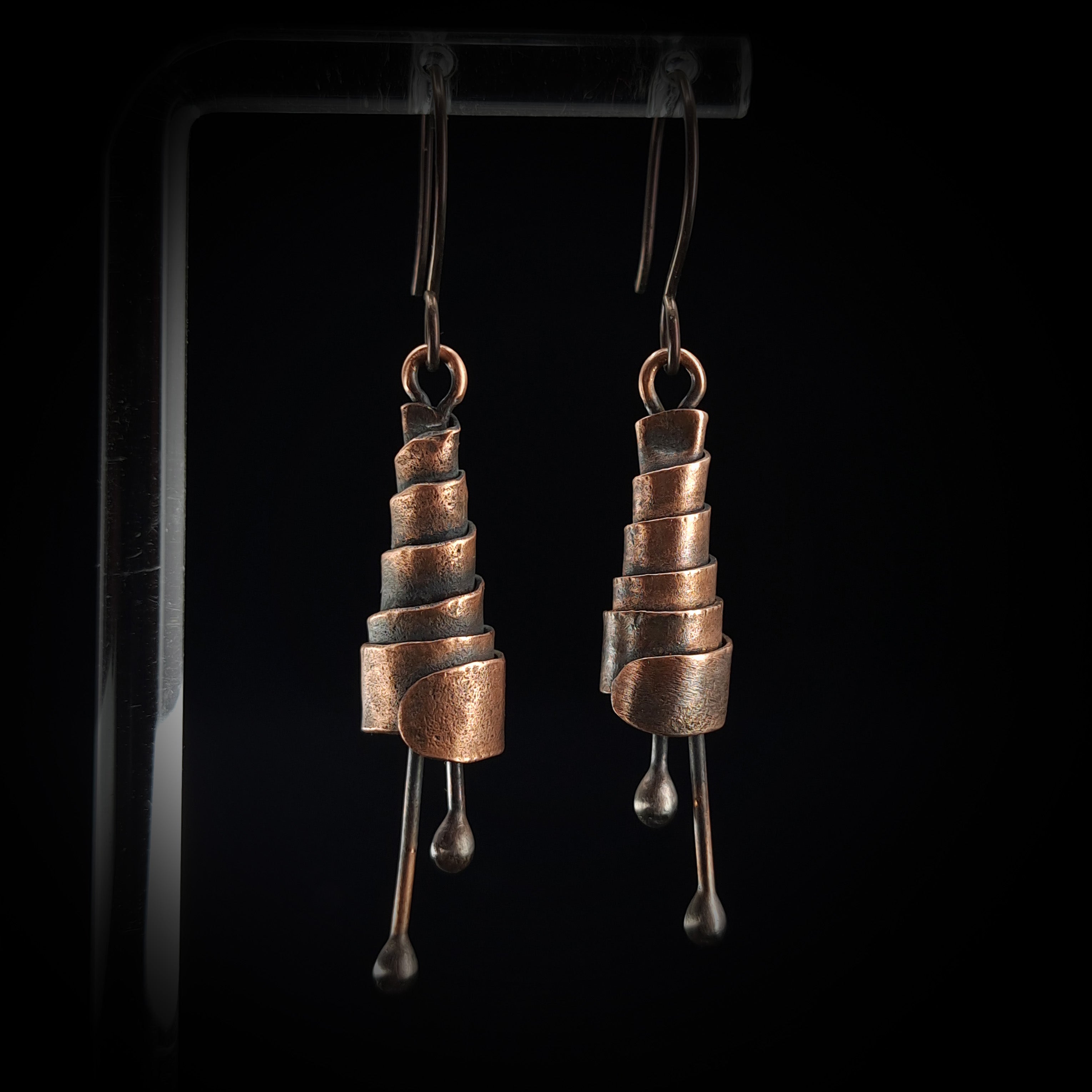 Copper spiral earrings close-up, black background — oxidized copper texture